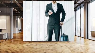 Happy young businessman walking and looking at mobile phone at airport. Handsome business executive texting on smartphone while walking in airport terminal. Wall mural